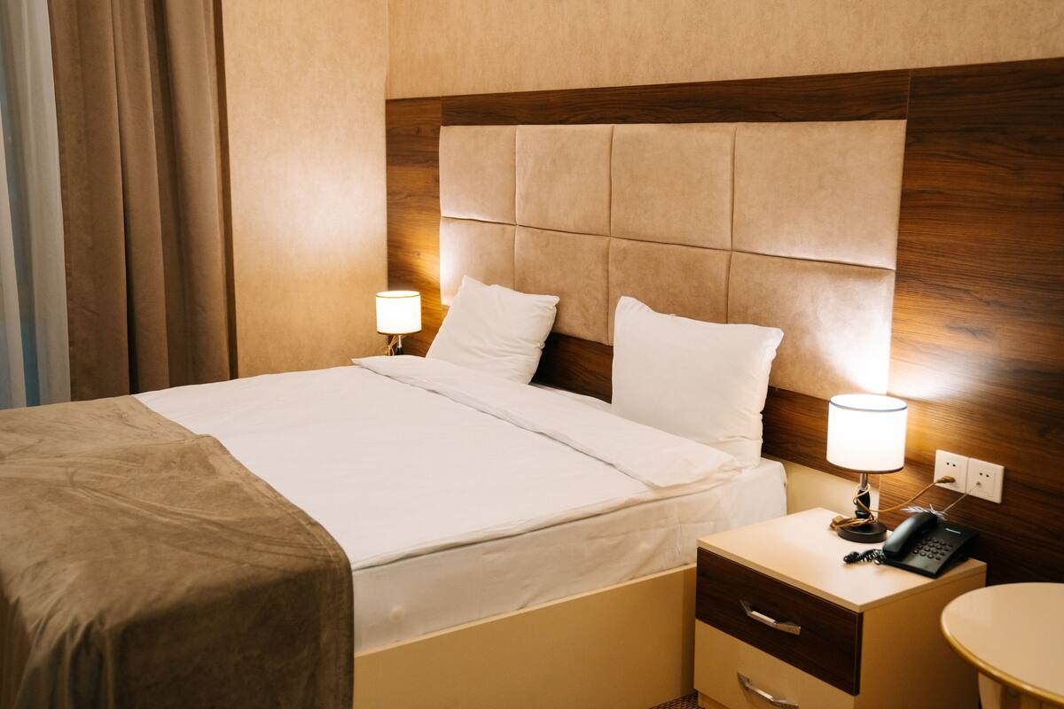 A hotel room with a bed, bedside table, lamp, and a phone.