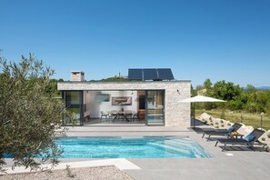 Une maison moderne dotée d’une piscine, de panneaux solaires et d’un espace repas avec mobilier d’extérieur.