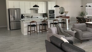 Une cuisine moderne avec des meubles blancs, un réfrigérateur en acier inoxydable et un îlot central doté de tabourets de bar.