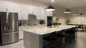 Une cuisine moderne avec des meubles blancs, des appareils en acier inoxydable et un grand îlot central doté de tabourets de bar.