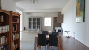 Un amplio salón con una estantería de madera, una mesa de comedor con sillas y una cocina al fondo.