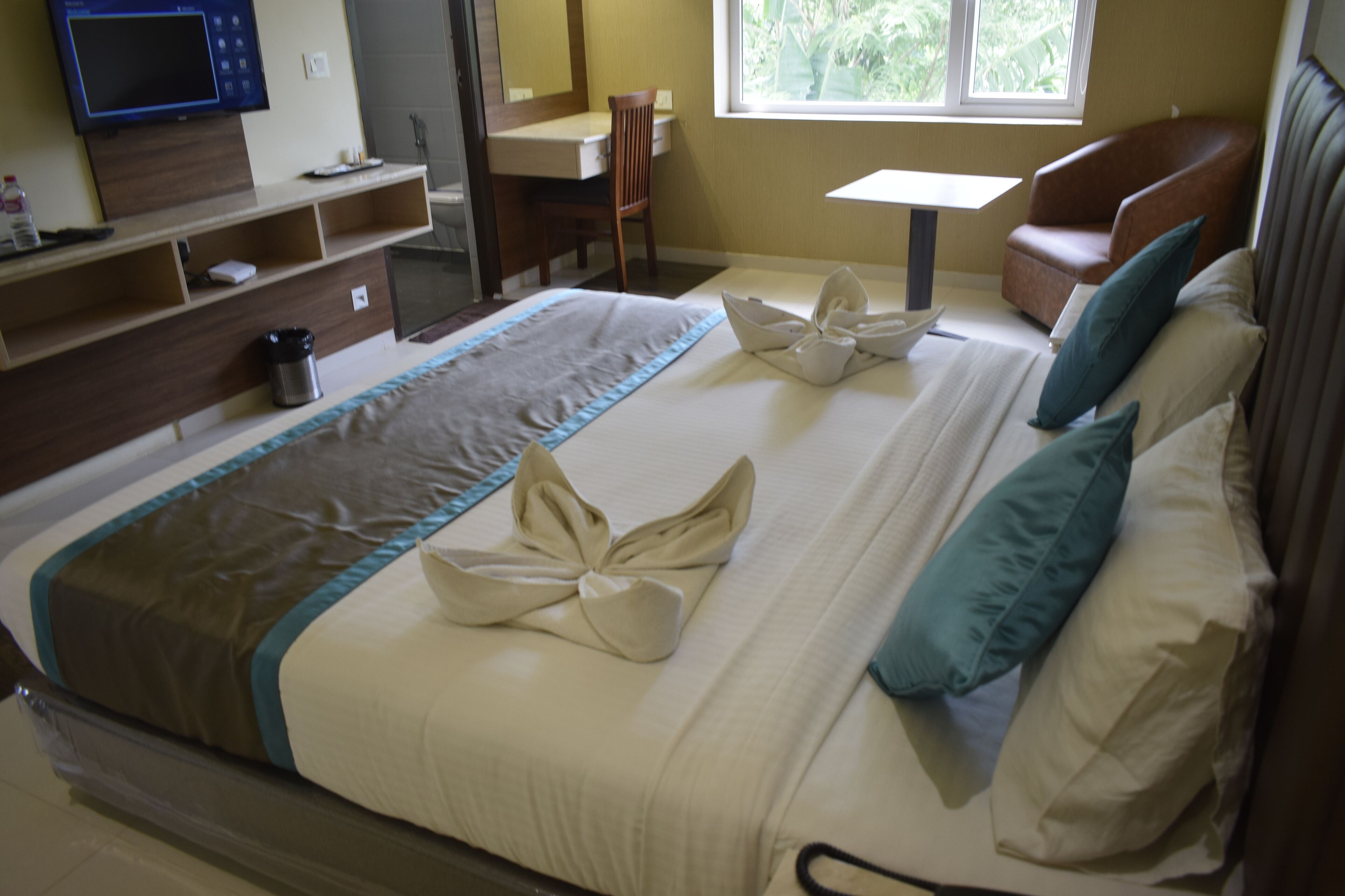 A hotel room with a bed, a desk, a chair, a TV, and a window.