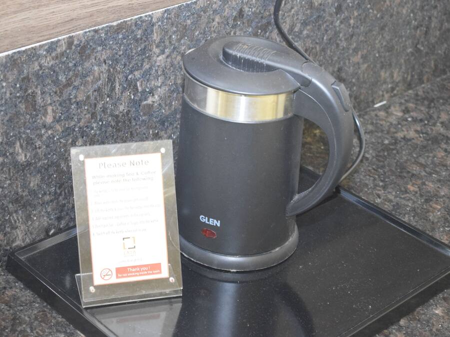 A black GLEN electric kettle on a granite countertop with a sign instructing not to smoke and to note the kettle's location.