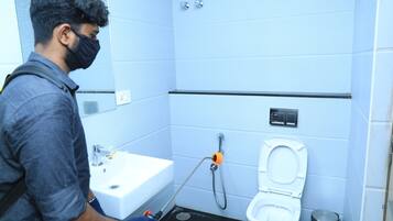 Una persona limpiando un baño con un pulverizador y una manguera.