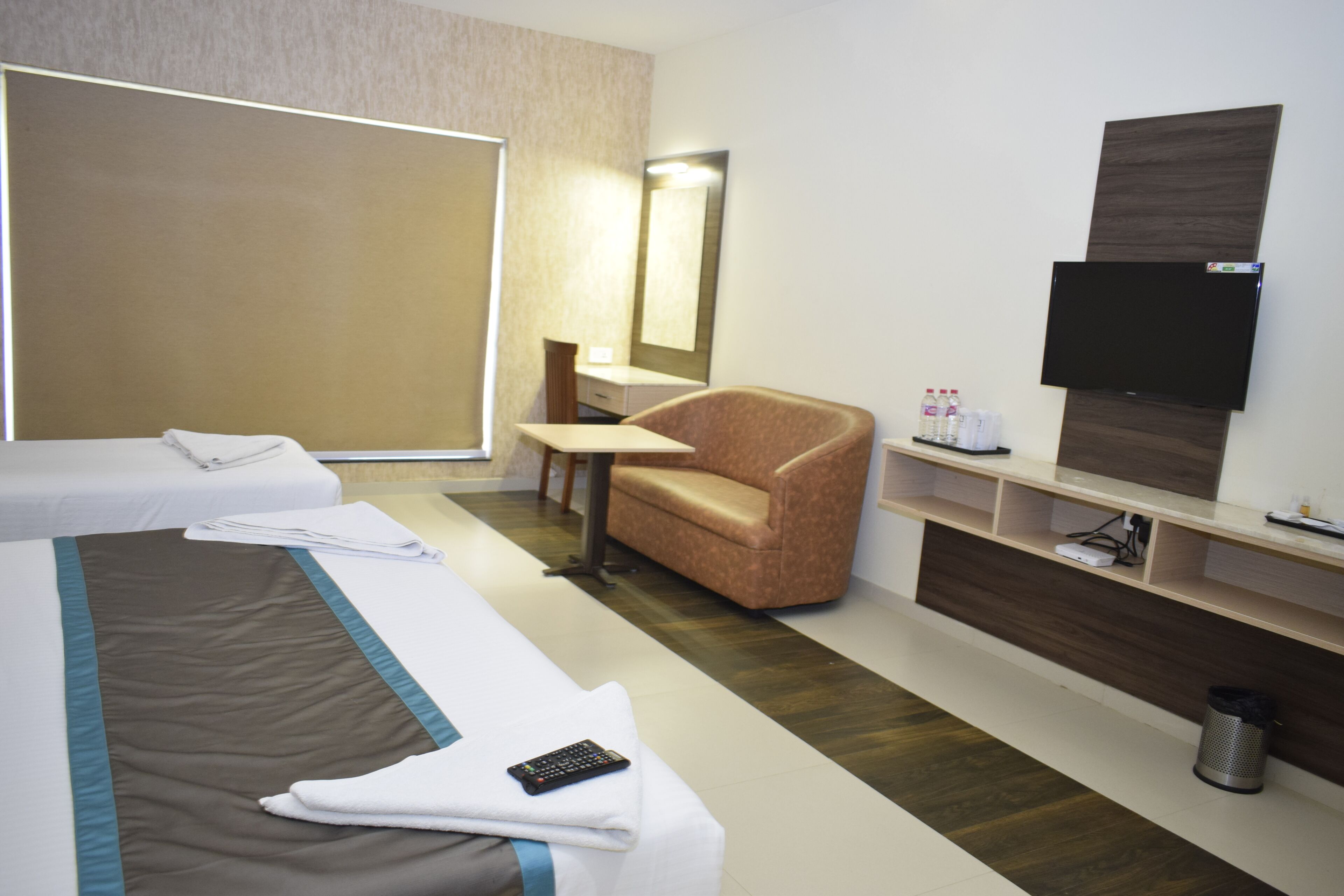 A hotel room with a bed, a chair, a TV, a small table, and a shelf with toiletries.