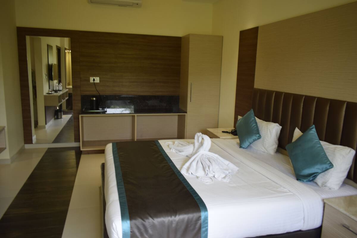 A hotel room with a large bed, a built-in desk, a mirror, and a kitchenette.