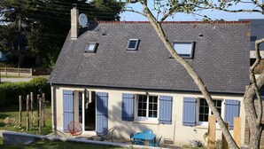 Ein zweigeschossiges Haus mit geneigtem Dach, Satellitenschüssel und zahlreichen Fenstern mit Fensterläden.