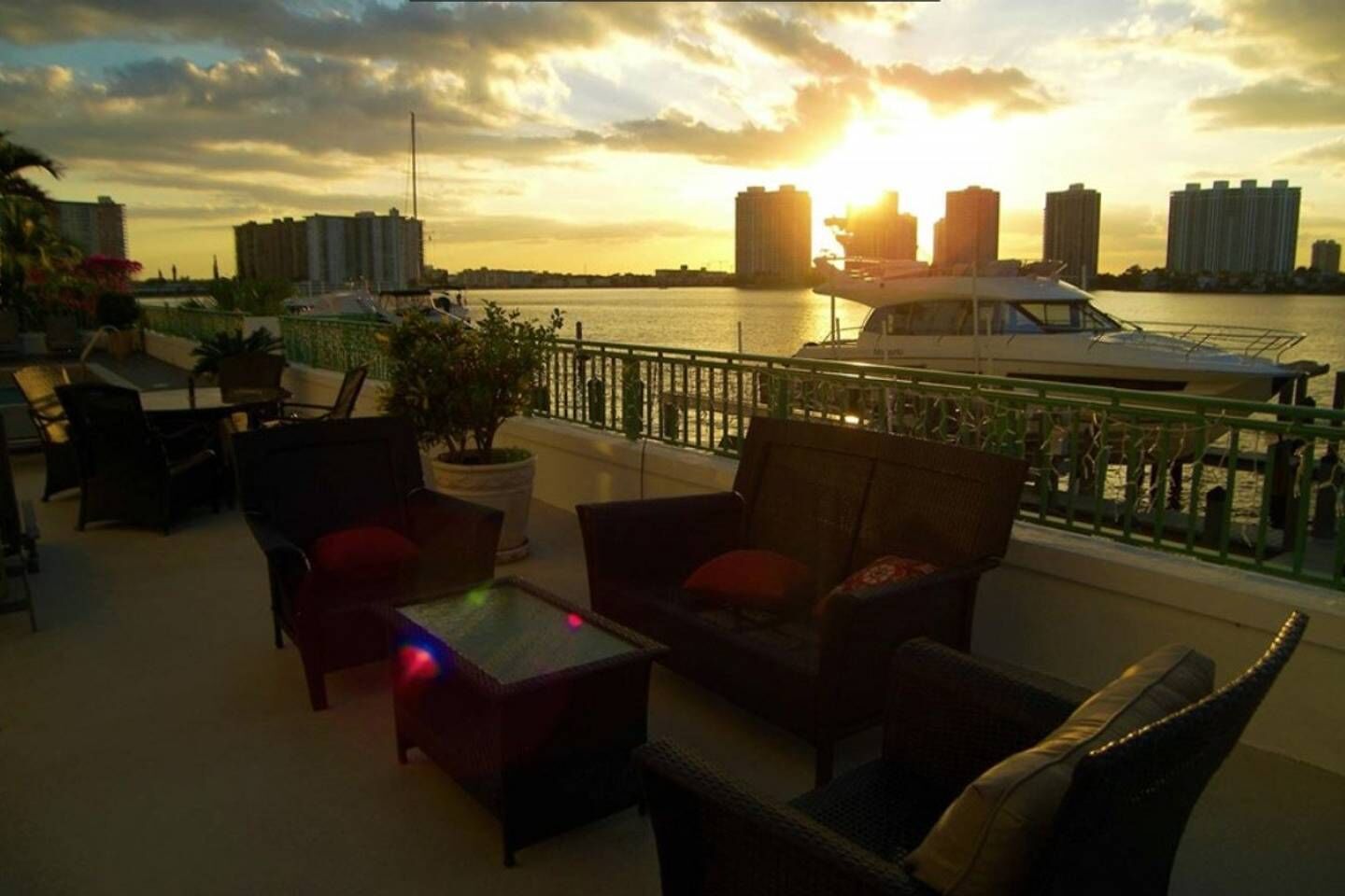 Eine Terrasse mit Sitzgelegenheiten im Freien, Blick aufs Wasser und Gebäude im Hintergrund.