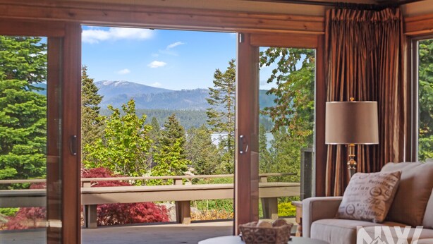 A room with a sliding glass door leading to a balcony with a mountain view. There is a sofa and a small table with a decorative bowl on it.