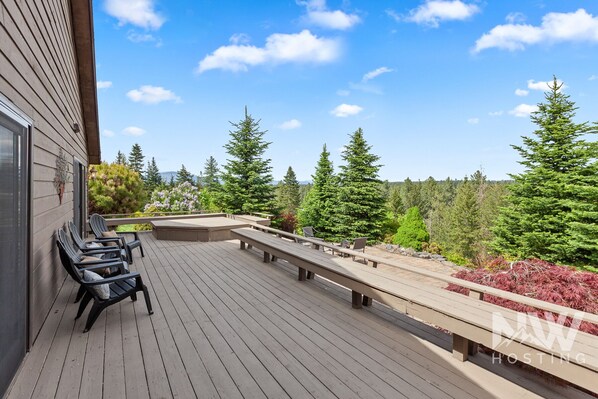 A wooden deck with outdoor seating, surrounded by trees and a clear sky. - Luxury Home—Fireplaces, Hot Tub, Fire Pit, Soaking Tub & Stunning Views for Ultimate Relaxation! (Hayden)
