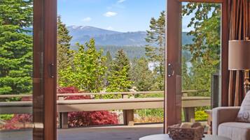 A room with a sliding glass door leading to a balcony with a mountain view. There is a sofa and a small table with a decorative bowl on it.