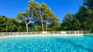 A clear blue swimming pool with a white fence and trees in the background.