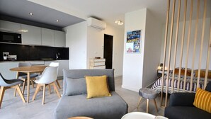 A modern living room with a grey sofa, a dining table with chairs, a small round table, and a bed with patterned bedding. - Large, newly renovated studio, quiet, 100 metres from the beautiful La Salis beach (Antibes)