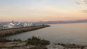 A marina with yachts docked, a stone breakwater, and a cityscape with mountains in the background. - Large, newly renovated studio, quiet, 100 metres from the beautiful La Salis beach (Antibes)