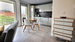 A modern kitchen with white cabinets, a dining area with a round table and chairs, and a view of a balcony with a railing. - Large, newly renovated studio, quiet, 100 metres from the beautiful La Salis beach (Antibes)