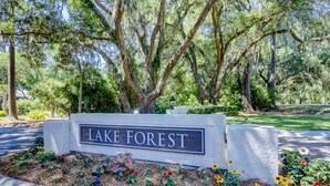 A sign reading "LAKE FOREST" surrounded by a landscaped area with various plants and flowers.