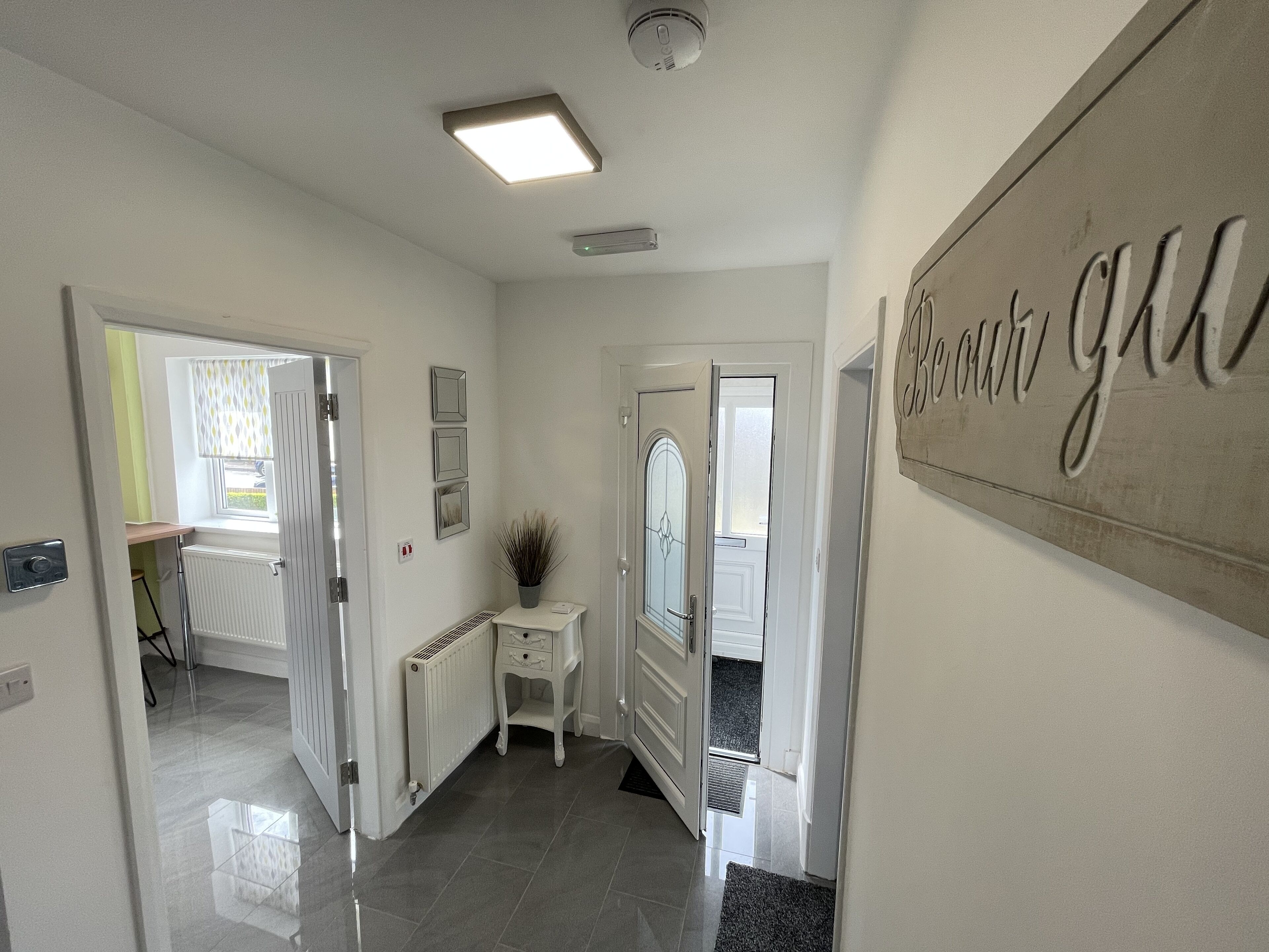 A hallway with a radiator, a small table with a plant, and a door with a sign.