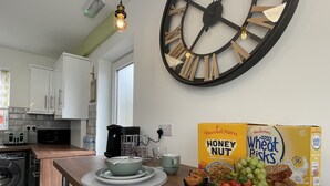 Eine Küche mit einer großen Wanduhr, einer Kaffeemaschine und Frühstücksartikeln, darunter Getreideflocken und Obst.