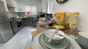 Eine moderne Küche mit grauen Schränken, einem eingebauten Backofen und einer Waschmaschine. Auf der Arbeitsfläche befinden sich Frühstücksgegenstände, darunter Obstteller und Getreideboxen.