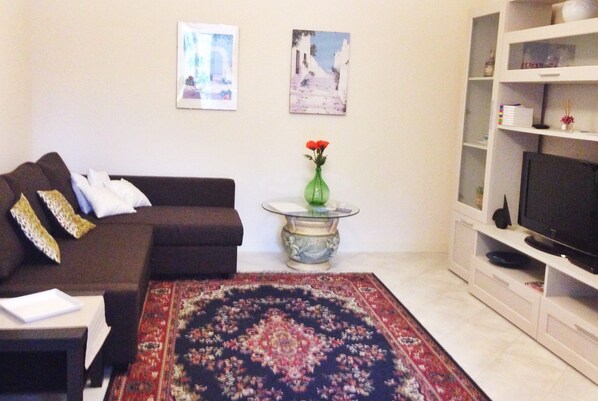 A living room with a sofa, a coffee table with a vase, a TV on a stand, and a patterned rug. - Crawford Home (Sant'Agnello)