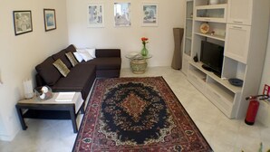 Een woonkamer met een bank, een salontafel, een vloerkleed, een televisie en een boekenkast.