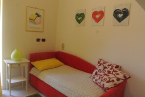 Un petit canapé rouge, agrémenté d’un coussin jaune et d’un autre à motifs, est placé contre un mur blanc. Trois décorations en forme de cœur ornent le mur.
