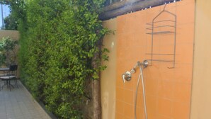 Een betegelde douche met een hangplankje, een betegelde vloer en een muur begroeid met groene planten.