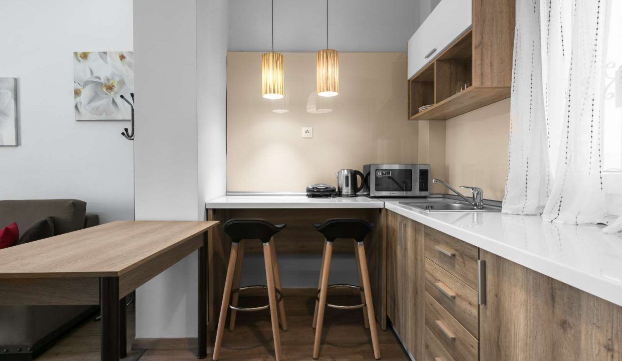 A modern kitchen with wooden cabinets, a white countertop, two bar stools, a coffee maker, and a microwave.