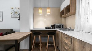 Une cuisine moderne avec des meubles en bois, un plan de travail blanc, deux tabourets de bar, une machine à café et un four à micro-ondes.