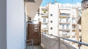 Un balcon doté d’une rambarde en métal, d’une chaise en bois et offrant une vue sur les bâtiments voisins.