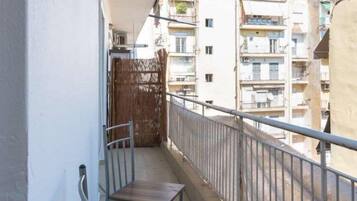 A balcony with a metal railing, a wooden chair, and a view of adjacent buildings.