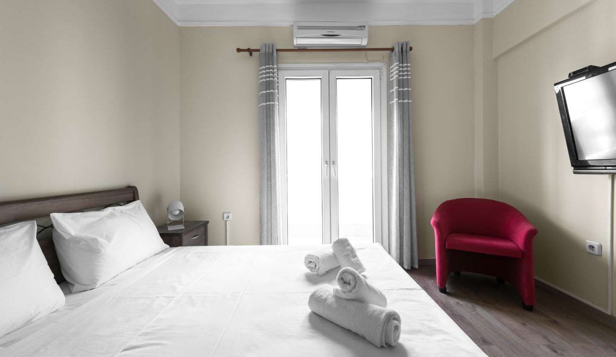 Una habitación de hotel con una cama, un sillón rojo, un televisor y una ventana con cortinas.