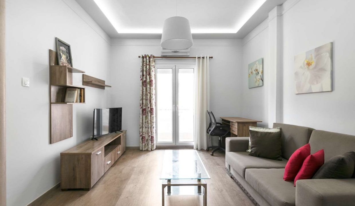 A modern living room with a sofa, coffee table, TV, and a desk with a chair.