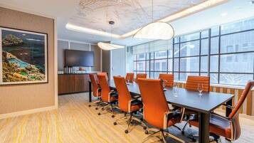 Un salón de conferencias con una larga mesa, sillas color naranja y un amplio ventanal con vistas a edificios.
