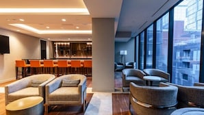Een moderne hotel lobby met zithoeken, een bar en grote ramen met uitzicht op de stad.