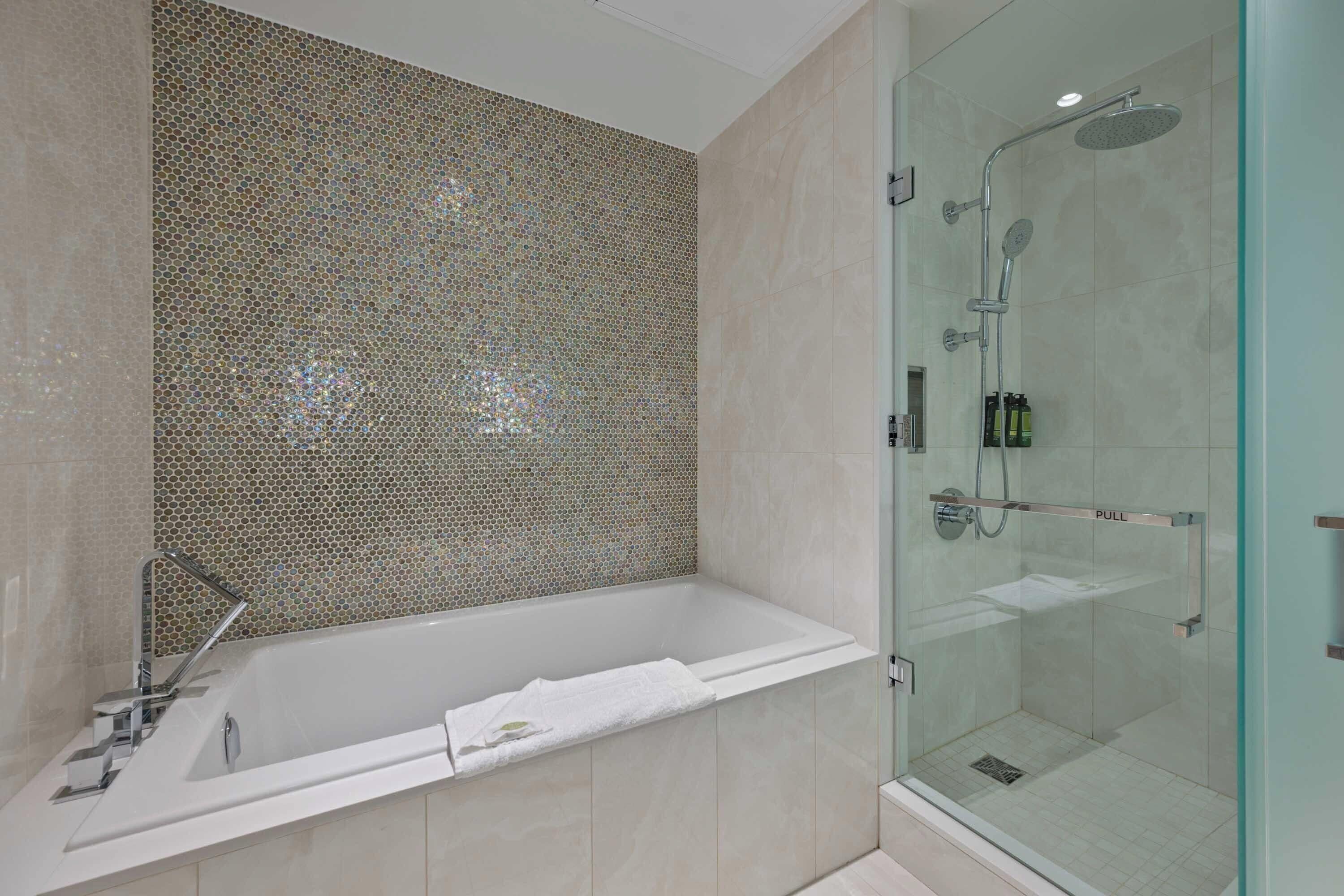 Un baño moderno con ducha de mampara de vidrio, una bañera independiente y un muro de mosaicos.