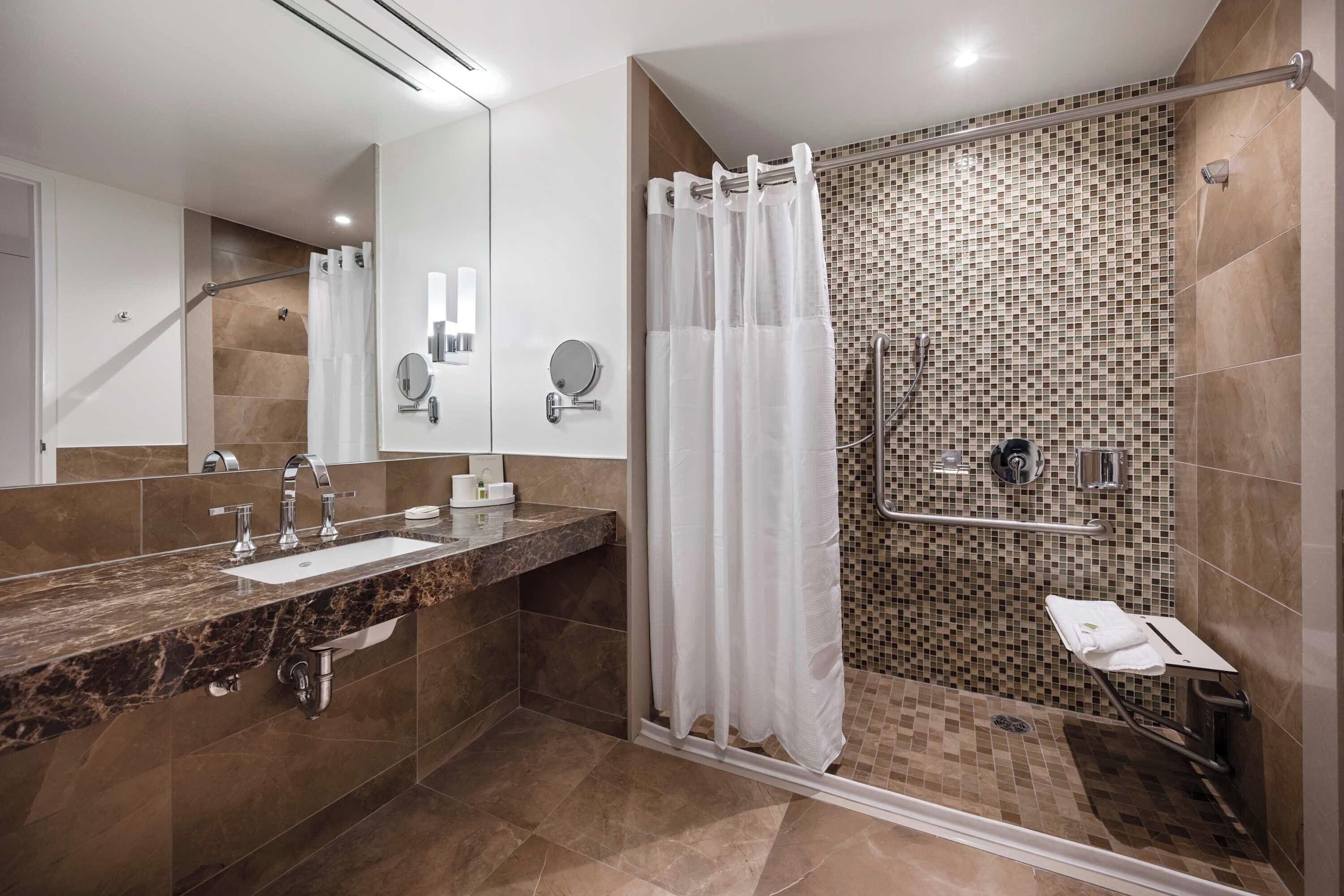 Un baño moderno con lavamanos de mármol, cabina de ducha de vidrio y pared de ducha con mosaicos.