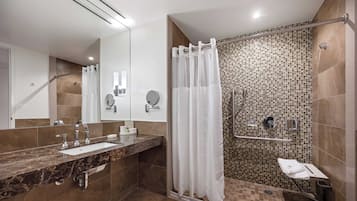 Un baño moderno con lavamanos de mármol, cabina de ducha de vidrio y pared de ducha con mosaicos.
