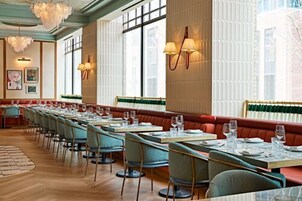 A restaurant with long tables, cushioned booths, and pendant lighting.