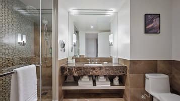 Un baño moderno con ducha envuelta en vidrio, lavabo de mármol y un inodoro.