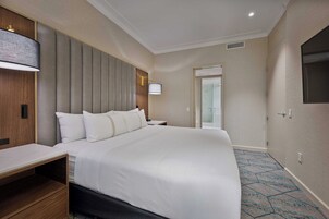 Een hotelkamer met een groot bed, een nachtkastje, een lamp en een aan de muur bevestigde televisie.