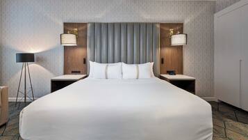 A large bed with a grey headboard, two bedside tables, two lamps, and a carpeted floor.