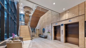 Een moderne lobby met een trap, zithoek en liften.
