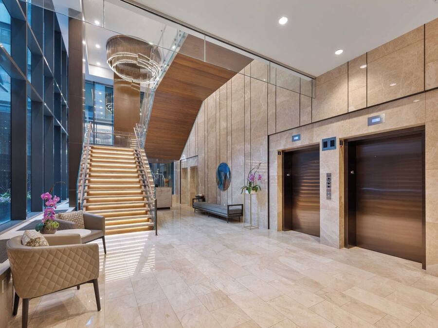 Een moderne lobby met een trap, zithoek en liften.