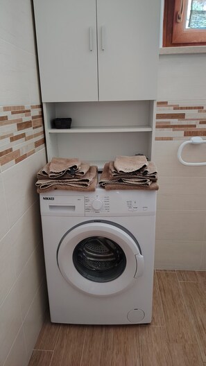 A front-loading washing machine with a control panel, stacked towels, and a cabinet above it. - Casa Giuditta, Nuovo e Indipendente Appartamento con Meravigliosa Vista Lago (Albisano di Torri del Benaco)