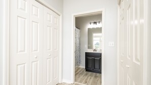 A hallway with white doors, a bathroom with a mirror and sink, and a shower with a patterned curtain.