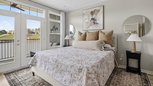 A bedroom with a bed, two bedside tables, a large window, and a door leading to a balcony.