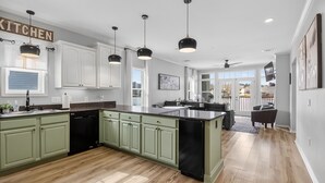 A spacious kitchen with green cabinets, a central island, and pendant lighting.