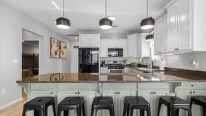 A modern kitchen with white cabinets, a granite countertop, and black bar stools.