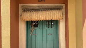 Una puerta verde con un felpudo tejido encima, una ventana pequeña y un picaporte de metal.